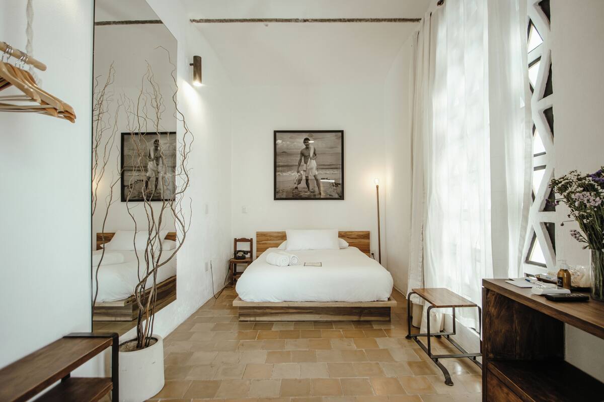 Un dormitorio con cama, mesita de noche, lámpara y un cuadro colgado en la pared.