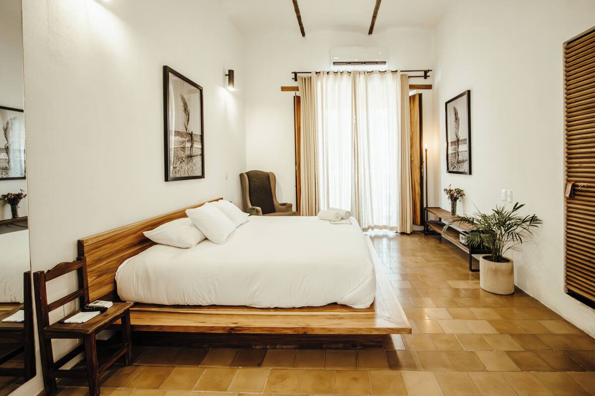 Un dormitorio con una cama de madera, una silla, un banco y una planta en maceta.