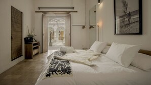 Un dormitorio moderno con una cama grande, un banco de madera, una planta en maceta y un cuadro en la pared.