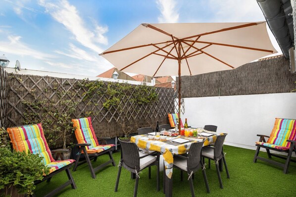 Een terras met een tafel, stoelen en een parasol.