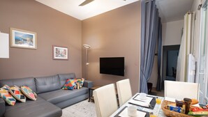A modern living room with a grey sofa, a dining table set for breakfast, and a flat-screen TV on the wall. - House Châteaudun - Air conditioning, Terrace & Private garage (Carcassonne)