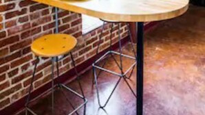 A brick wall with a round mirror, a wooden table with a bowl of fruit, and a stool. - Evie's apartment (Oklahoma City)