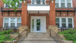 A two-story brick building with a central entrance, stone steps, and a small balcony with a railing. - Evie's apartment (Oklahoma City)