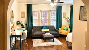 A living room with a sofa, armchair, and ottoman, a dining area with a table and chairs, and a ceiling fan. - Evie's apartment (Oklahoma City)