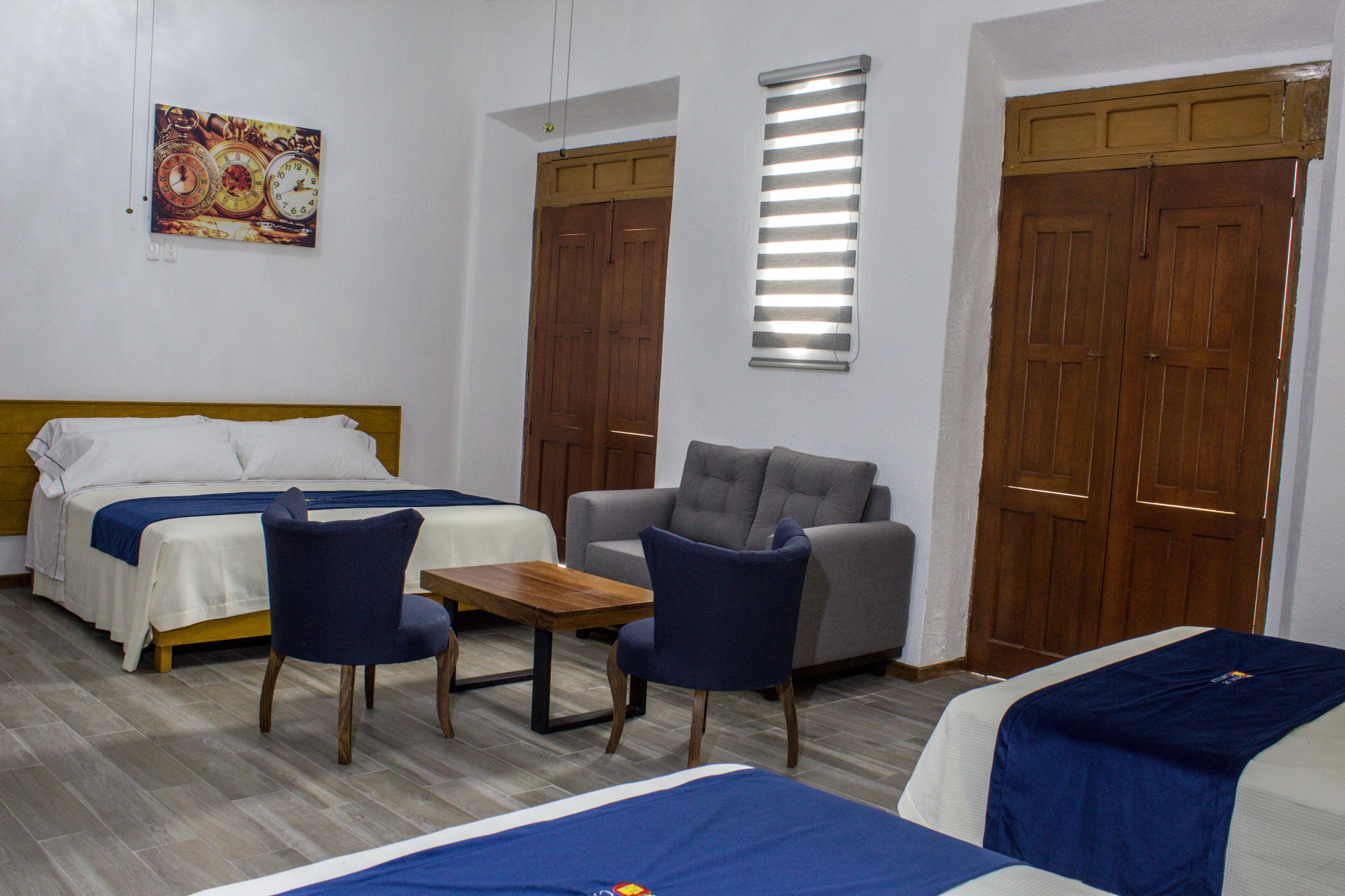 A hotel room with two beds, a sofa, a table, and a clock on the wall.