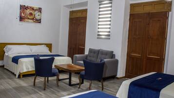 A hotel room with two beds, a sofa, a table, and a clock on the wall.