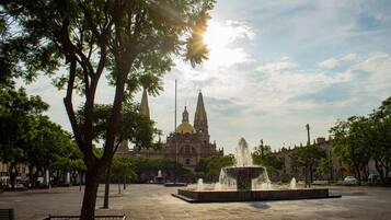 Una plaza con una fuente, árboles y un edificio histórico con cúpula y agujas al fondo.
