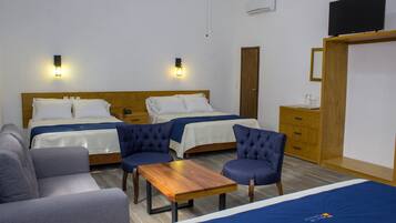Quarto de hotel com duas camas, um sofá, uma mesa e uma televisão.