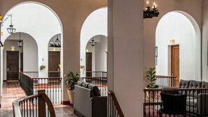 Eine geräumige Lobby mit einer imposanten Treppe, einer Sitzecke mit Sofas und einem Esstisch, und einem großen, bogenförmigen Durchgang zu einem weiteren Raum.