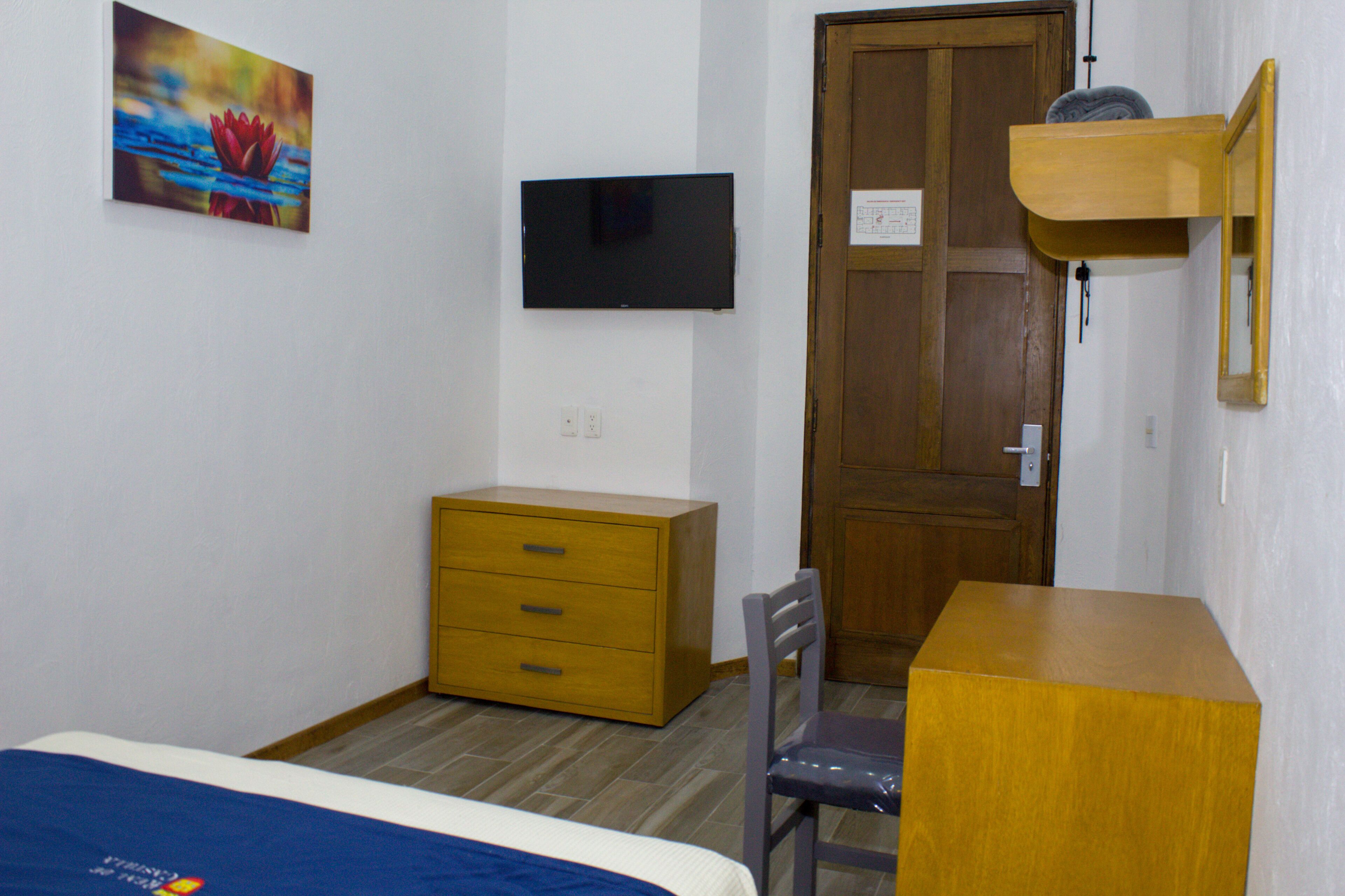 Ein Schlafzimmer mit einem Bett, einer Holzkommode, einem Schreibtisch, einem Stuhl, einem Fernseher und einer Tür.