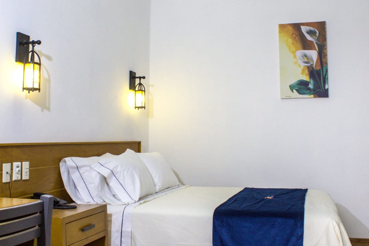Habitación de hotel impecable con cama, mesita de noche, lámpara y un cuadro en la pared.