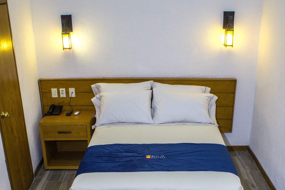 Una habitación de hotel con una cama, mesitas de noche, un escritorio y una silla.