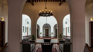 Eine prächtige Eingangshalle mit einer Kronleuchter, gewölbter Decke und Blick auf eine untere Ebene mit Sitzgelegenheiten und Pflanzen.