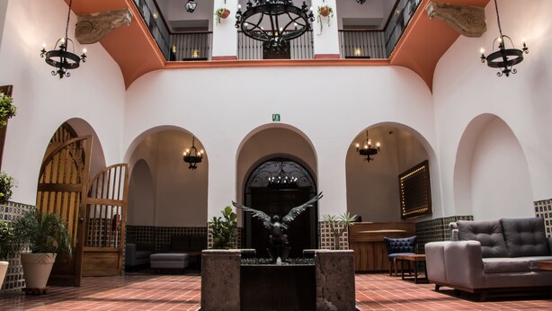 Eine geräumige Lobby mit einer zentralen Fontäne, Sitzbereichen und einer Treppe zu einer oberen Ebene.
