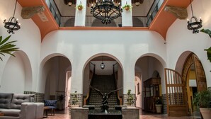 Ein großzügiger Innenhof mit einer zentralen Treppe, zahlreichen Bögen, hängenden Kronleuchtern und Kübelpflanzen.
