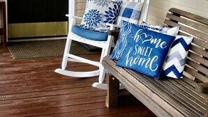 Eine hölzerne Veranda mit einem Schaukelstuhl und einer Bank, beide mit Zierkissen.