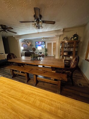A dining area with a wooden table and benches, a ceiling fan, a television, and a cabinet with glass doors.