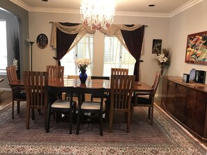 Uma sala de jantar com uma mesa redonda de madeira, cercada por cadeiras, um candelabro e um tapete estampado.