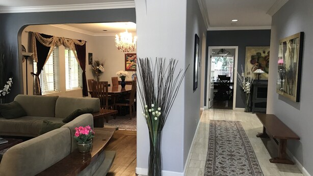 Sala de estar com sofá, mesa de centro e um vaso com flores. Há uma área de jantar com mesa e cadeiras, e um corredor com tapete e um banco.