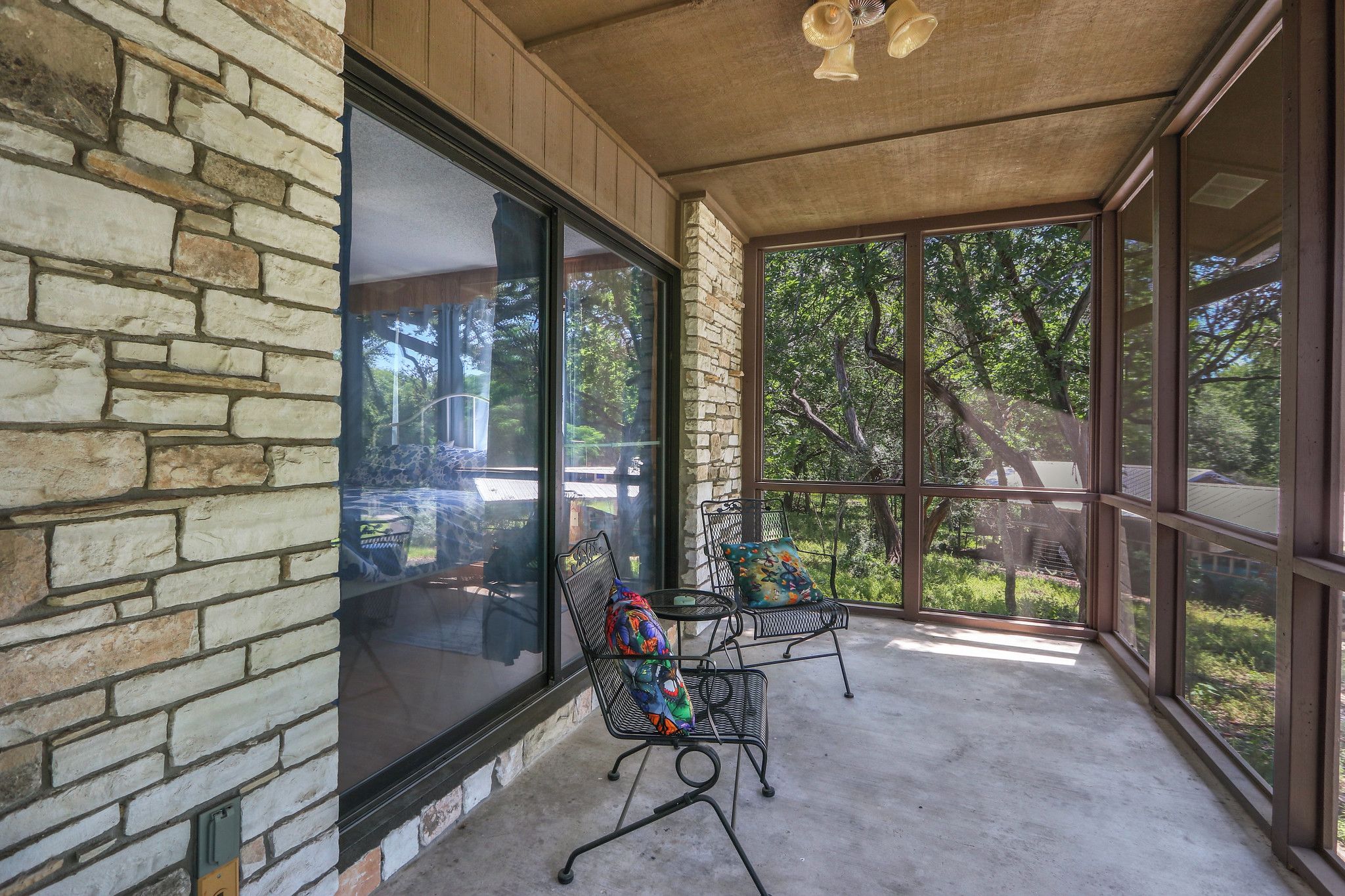 A covered patio with a stone wall, large windows, and outdoor furniture.