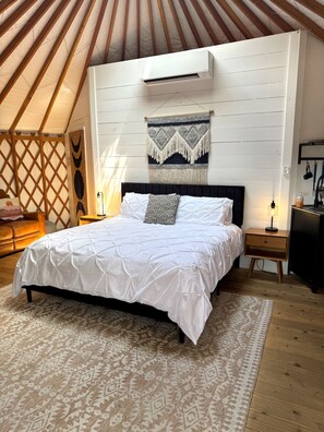 Un dormitorio con cama, aire acondicionado de pared, alfombra estampada y suelo de madera.