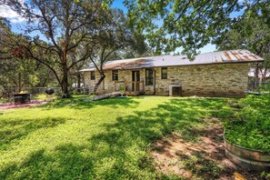 A stone building with a metal roof, surrounded by a grassy yard and trees. - Charming 2 bedroom house in the heart of Downtown Wimberley! Walk to the Square! (Wimberley)