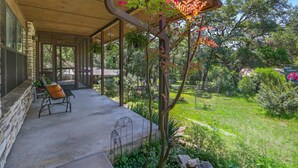 Une véranda abritée avec une chaise, des murs en pierre et un jardin où poussent différentes plantes et fleurs.
