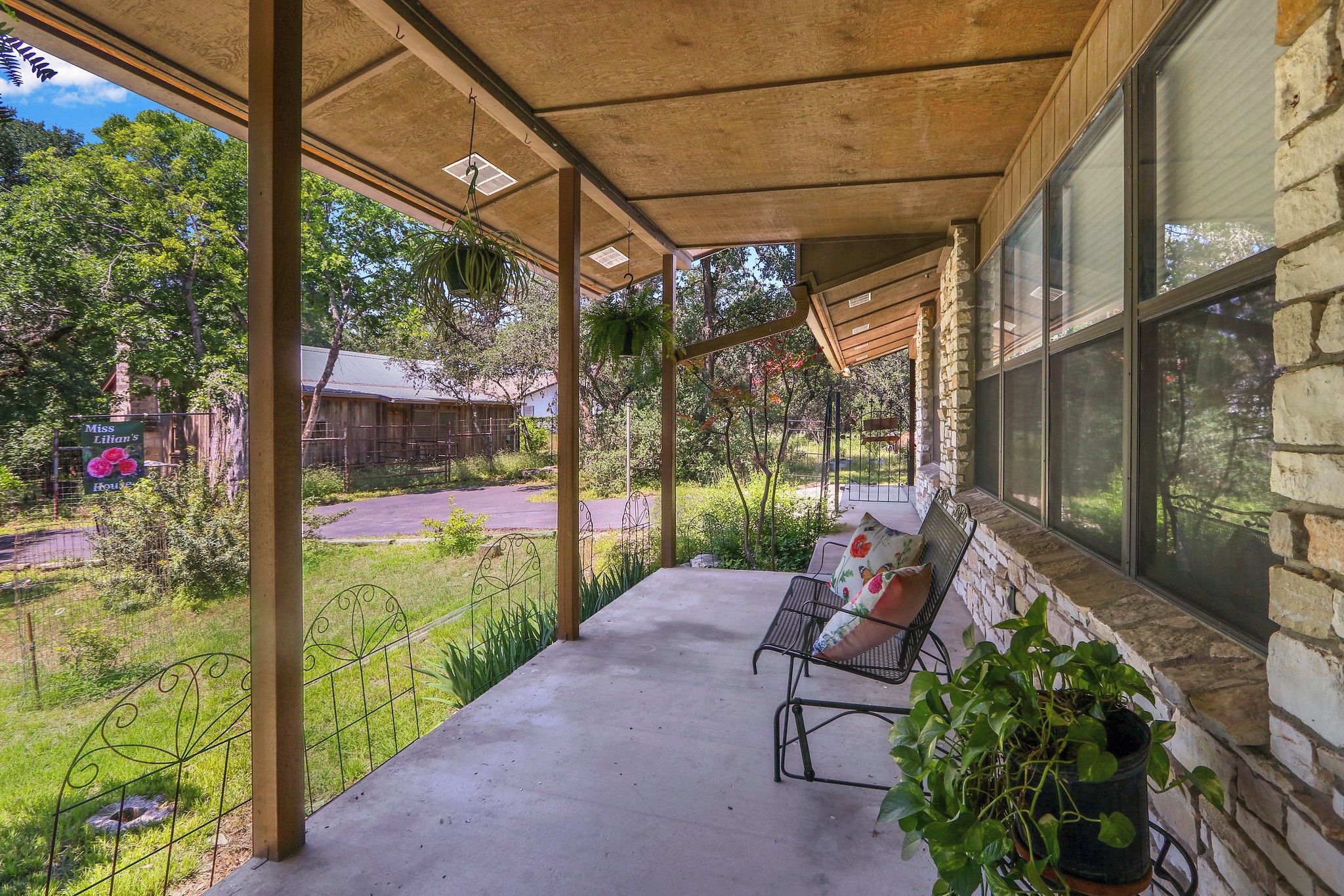 Un porche cubierto con un banco y plantas en macetas, con vistas a una zona verde y un edificio.