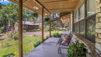Une véranda avec un banc et des plantes en pot, donnant sur une pelouse et un bâtiment.