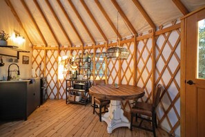 Un interior acogedor con una mesa y sillas de madera, una zona de cocina con un lavamanos y electrodomésticos, y un diseño de pared con celosía.