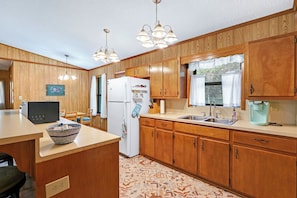 Una cocina con armarios de madera, un refrigerador, un fregadero y una zona de comedor con una mesa y sillas.