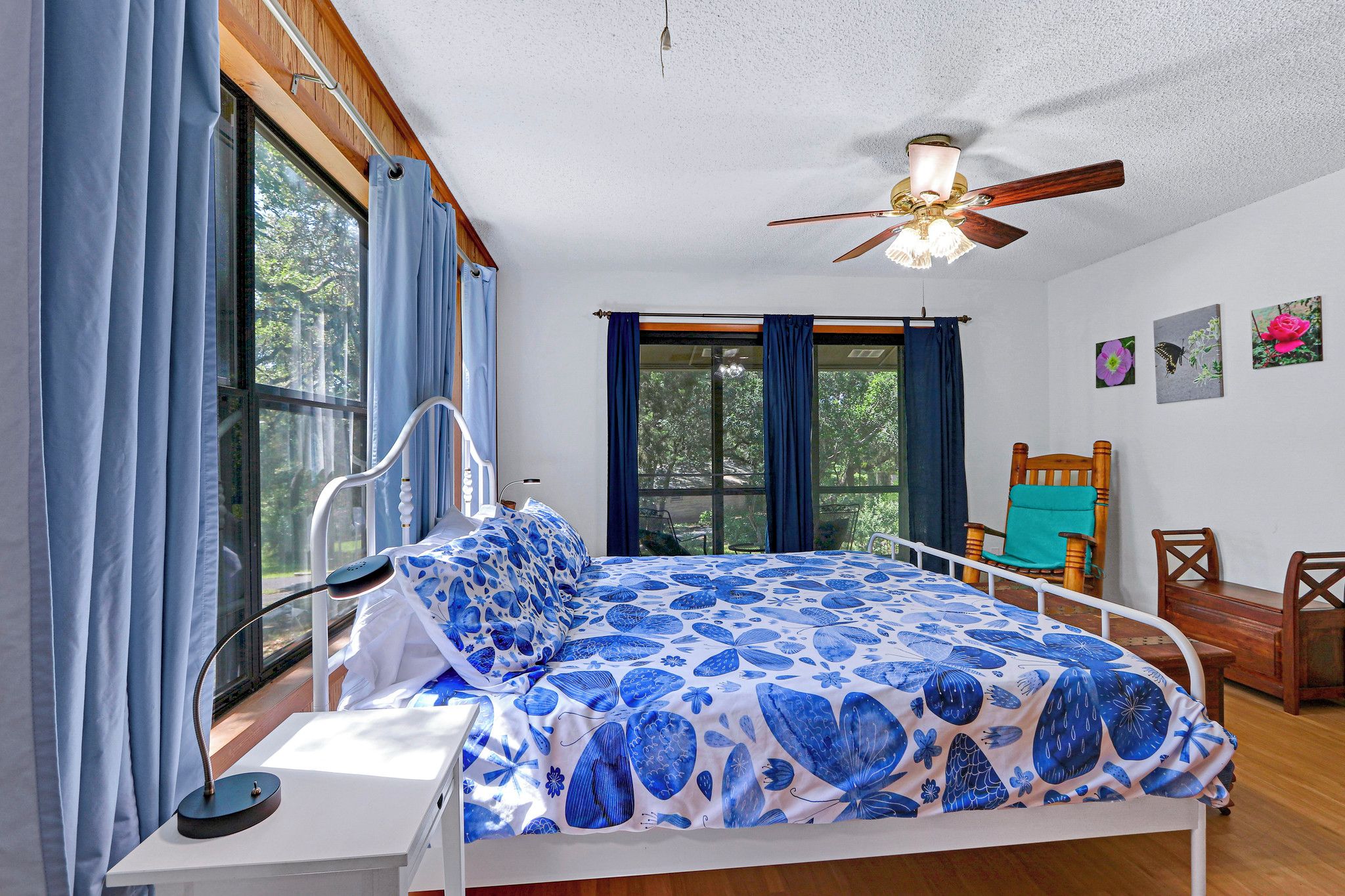 A bedroom with a bed, a ceiling fan, a window with curtains, and a wall with pictures.
