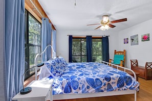 Un dormitorio con cama, ventilador de techo, ventana con cortinas y pared con cuadros.
