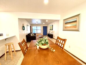 A dining area with a wooden table, chairs, a sofa, and a potted plant. - Garage Studio near OUSHC Hospital (Oklahoma City)