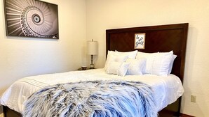 A neatly made bed with a fluffy white and blue throw blanket, a wooden headboard, and a wall-mounted picture frame with a spiral design. - Garage Studio near OUSHC Hospital (Oklahoma City)