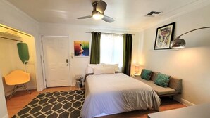 A bedroom with a bed, a sofa, a desk, a chair, a ceiling fan, and a painting on the wall. - Ar`s Artsy Downtown Bungalow 5 (Phoenix)