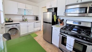 A compact kitchen with white cabinets, a stainless steel refrigerator, a microwave, a stove, and a washing machine. - Ar`s Artsy Downtown Bungalow 5 (Phoenix)