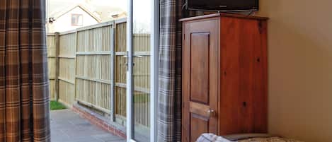 Quarto com cama, guarda-roupa de madeira, televisão sobre um suporte e porta de vidro deslizante que dá para um alpendre.