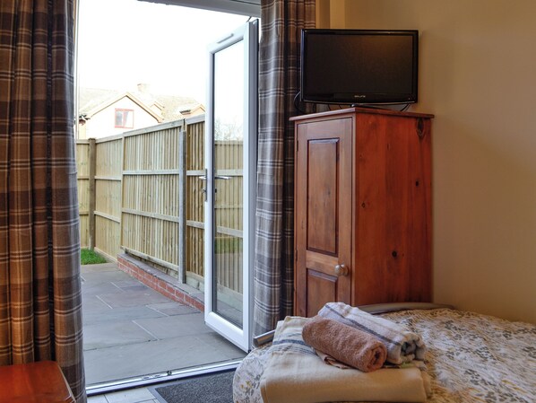 A bedroom with a bed, a wooden wardrobe, a television on a stand, and a sliding glass door leading to a patio.
