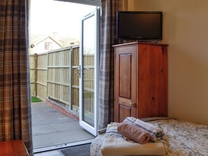 Een slaapkamer met een bed, een houten kledingkast, een televisie op een standaard en een glazen schuifdeur die uitkomt op een terras.