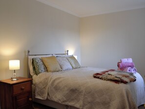 A neatly made bed with a patterned bedspread, a bedside lamp, and a stack of towels.