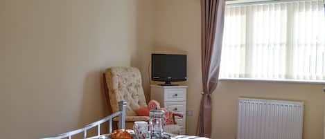 A bedroom with a bed, a television on a stand, a radiator, and a window with curtains.