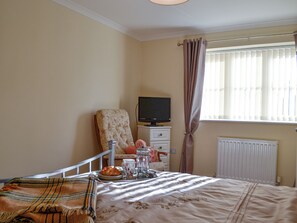 Een slaapkamer met een bed, een televisie op een standaard, een radiator en een raam met gordijnen.