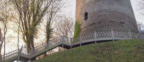 A stone tower with a staircase leading up to it, surrounded by trees and a grassy area.
