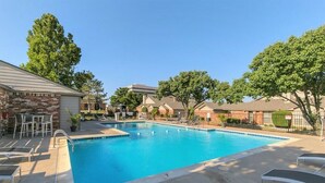 A swimming pool with lounge chairs and a brick building in the background. - Private Bedroom Suite - Communal House near Integris Private (Oklahoma City)