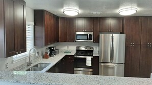 A modern kitchen with dark wood cabinets, stainless steel appliances, granite countertops, and a built-in microwave. - Private Bedroom Suite - Communal House near Integris Private (Oklahoma City)