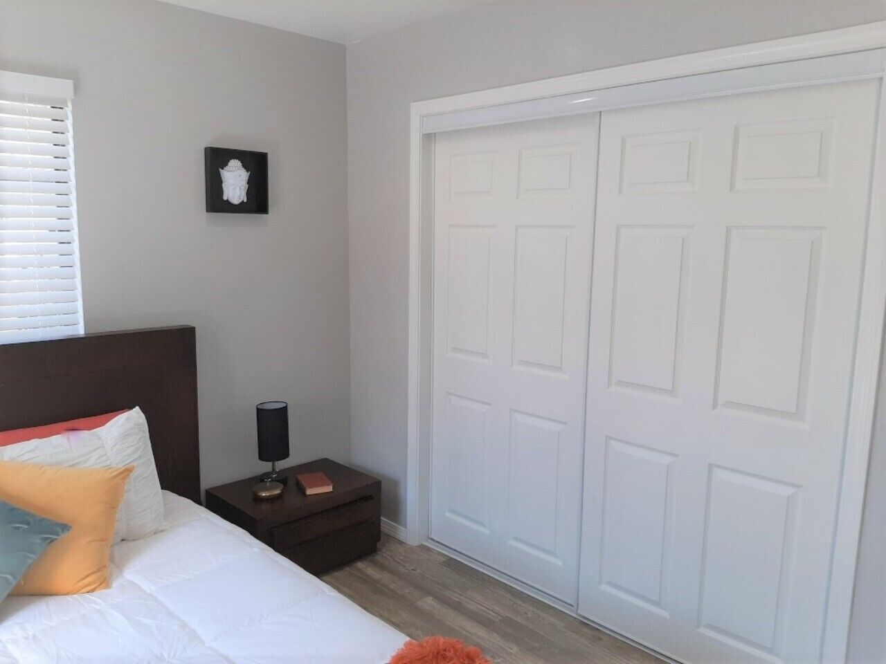 A bedroom with a bed, nightstand, lamp, and a white closet.