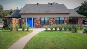 A two-story brick house with a blue front door, a covered porch, and a well-maintained lawn. - Private Bedroom Suite - Communal House near Integris Private (Oklahoma City)
