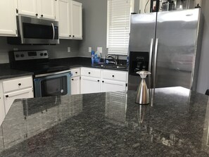 A kitchen with white cabinets, a stainless steel refrigerator, a microwave, an oven, and a granite countertop.