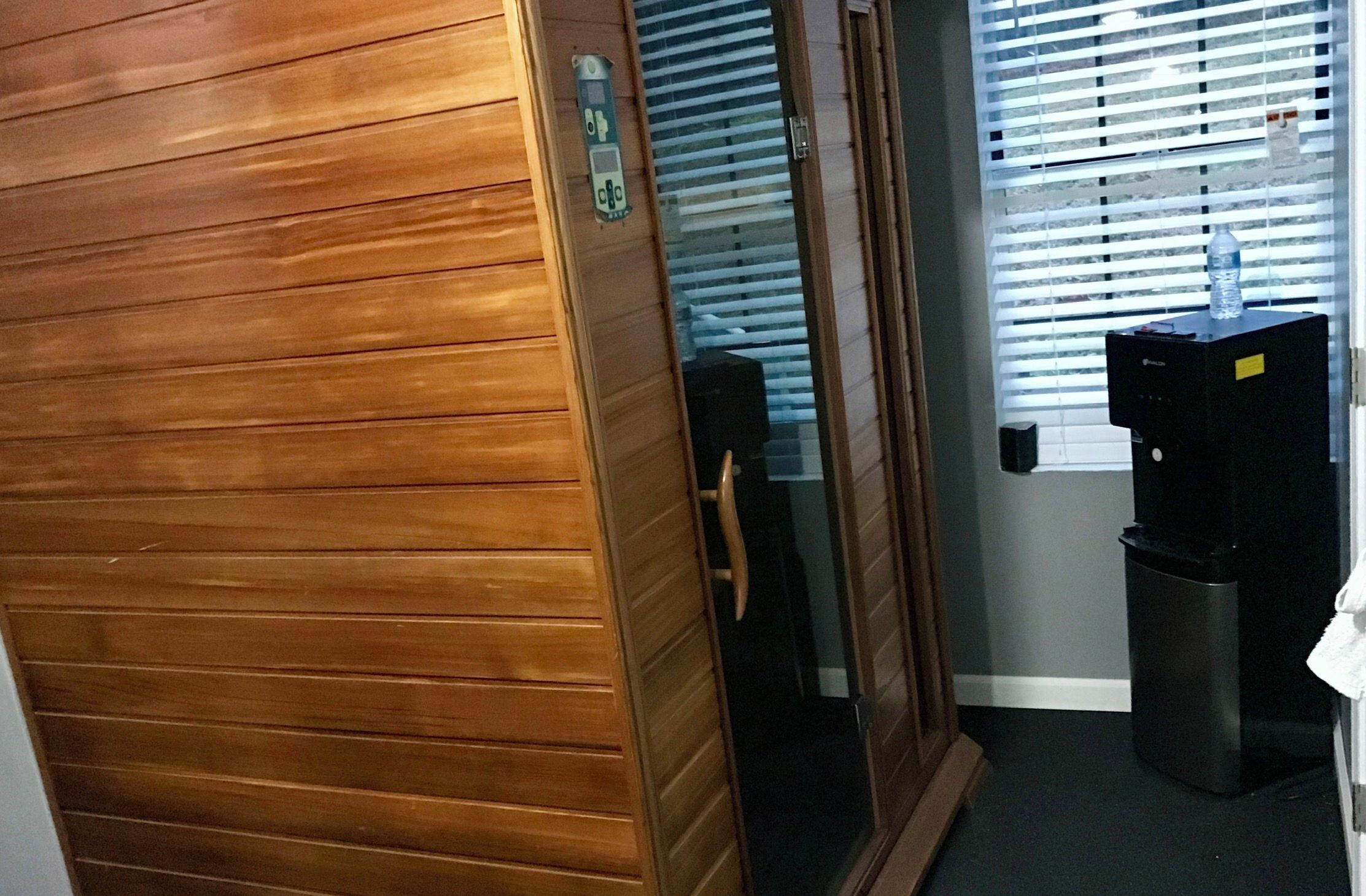 A hallway with a wooden door, a water dispenser, and a trash bin.